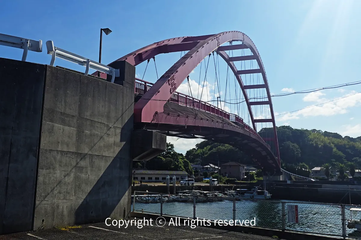 구찌노쓰항 입구에 놓인 붉은 아치교인 난반대교(Nanban Bridge / 南蛮大橋) 항구 부두와 방파제 옆에서 붉은 아치 트러스 구조와 교각 전체를 비스듬히 담은 와이드 뷰
